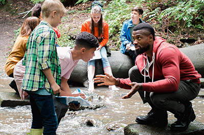 Picture at a brook in the forest, one sees children and an educator, who explains to them something, in addition the lettering "What look in the future conferences? We have suggestions!"