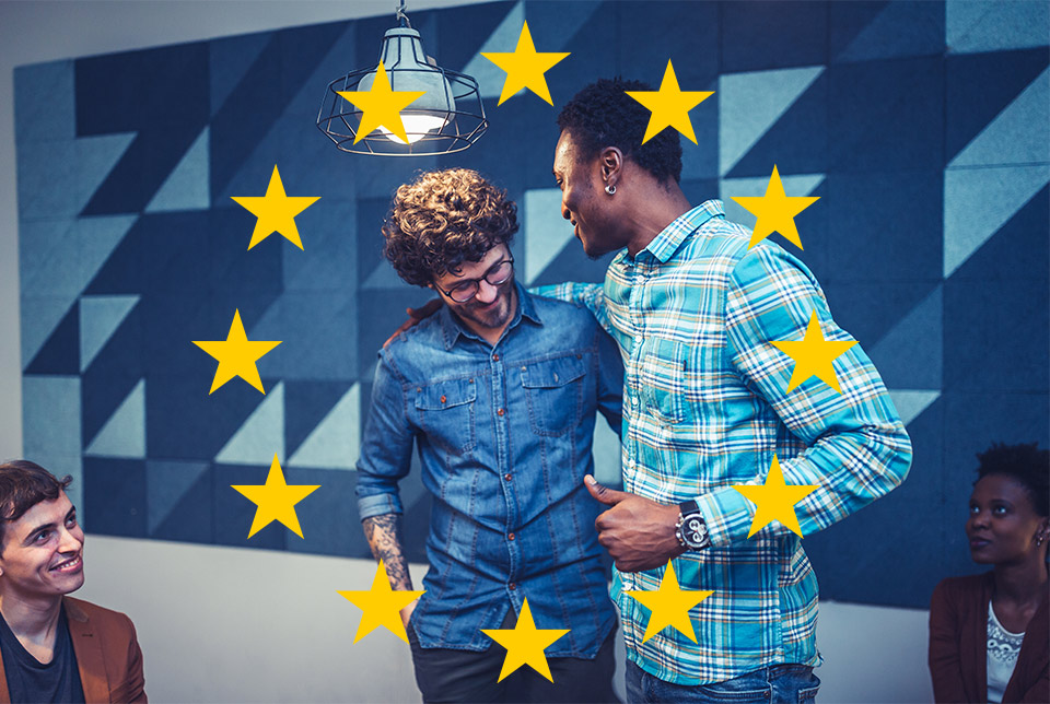 zwei Personen umarmen sich beherzt, umrahmt von EU-Sternen, während andere Konferenzteilnehmende zuschauen und sich darüber freuen