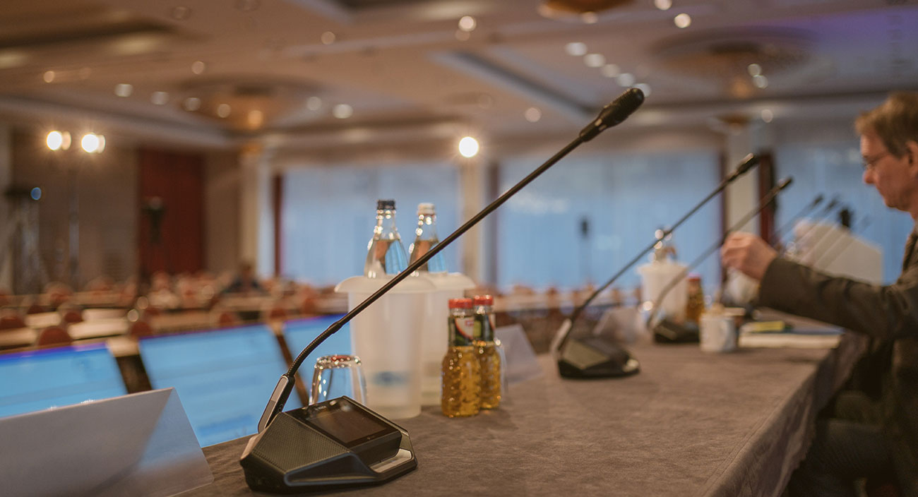 На U-образном конференц-столе расположены микрофоны, чтобы каждый член делегации мог говорить со своего места