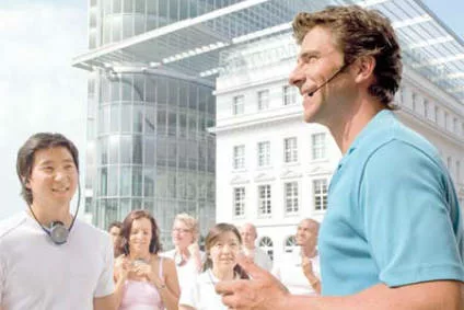 Man speaks into microphone, spectator listens with tour guide system during a tour. Rent, buy, lease personal tour systems at PCS.